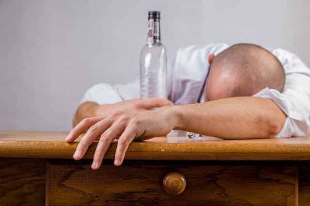 A drunk man with an alcohol bottle sleeping on a desk 