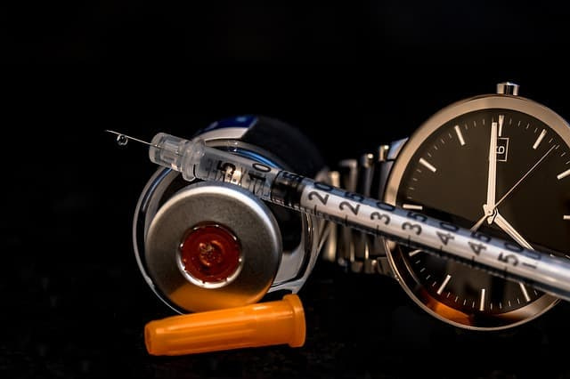 A syringe with an insulin bottle and a watch 