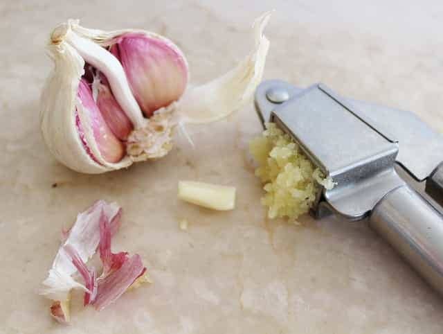 A half garlic bulb with a garlic press and crushed garlic 